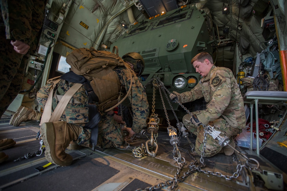 Air Force Senior Airman Brandon Lowe (right), a loadmaster with the 9th Special Operations Squadron, and Marine Corps Sgt. Jeffery Hale (left), a launcher chief with Kilo Battery, 2nd Battalion, 14th Marine Regiment, chain down a Marine Corps an M142 High Mobility Artillery Rocket System (HIMARS) onto an Air Force MC-130 at Fort Campbell, Ky., March 29, 2018. Marines from Kilo Battery flew from Fort Campbell to Dugway Proving Grounds, Utah, where they offloaded and fired four HIMARS missiles, demonstrating a unique capability that will give commanders more options to deal with threats when other options are not appropriate. (Marine Corps photo by Lance Cpl. Niles Lee)