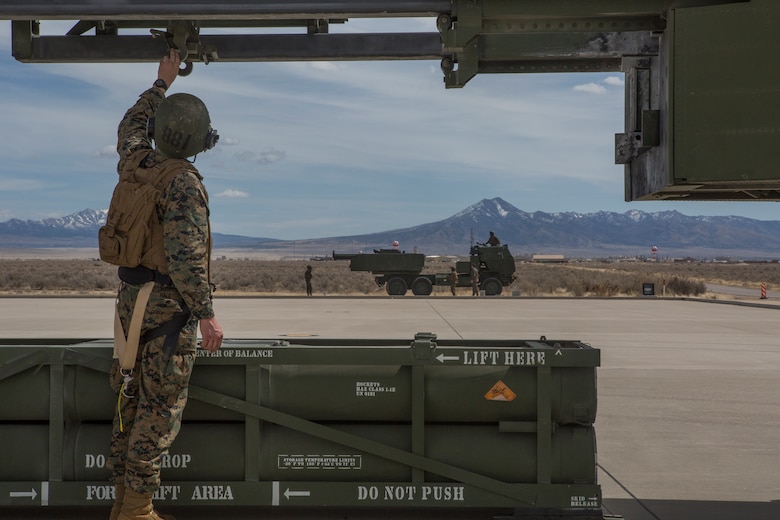 Marine Corps Sgt. Jeffery Hale, a launcher chief with Kilo Battery, 2nd Battalion, 14th Marine Regiment, guides a hoist up on an M142 High Mobility Artillery Rocket System (HIMARS) after dropping off a missile pod, at Dugway Proving Grounds, Utah, March 30, 2018. Marines from Kilo Battery flew from Fort Campbell, Ky., to Dugway where they offloaded and fired four HIMARS missiles, demonstrating a unique capability that will give commanders more options to deal with threats when other options are not appropriate. (Marine Corps photo by Lance Cpl. Niles Lee)