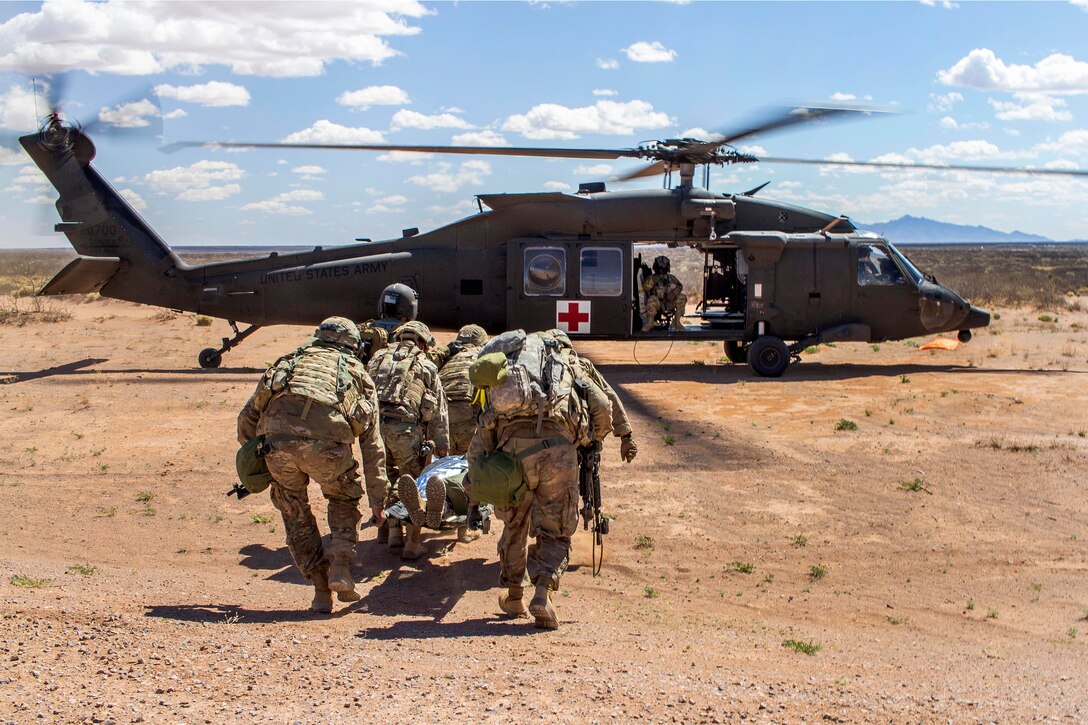 Soldiers transport a mock patient on a stretcher to a helicopter.