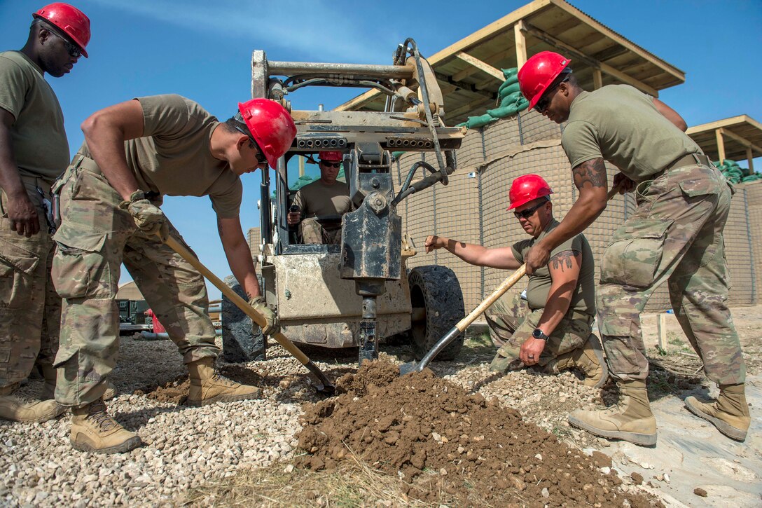 Soldiers shovel dirt from a hole.