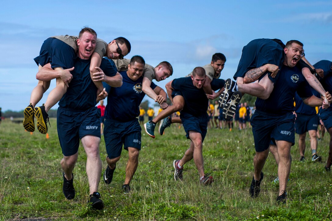 Sailors run on a field while carrying fellow sailors slung over their shoulders.