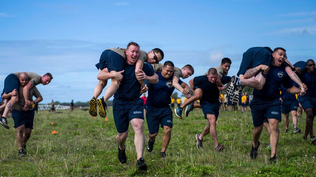 Sailors run on a field while carrying fellow sailors slung over their shoulders.