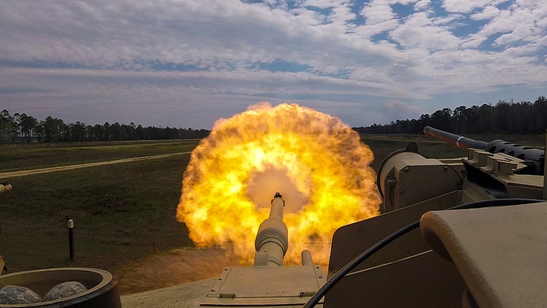 A fireball erupts out of the gun of a tank.