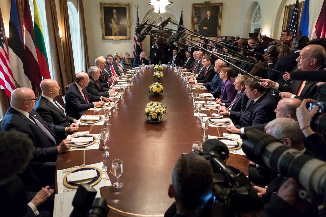 President Donald J. Trump sits at an oval table with other officials as media personnel hold microphones in the center of the table.
