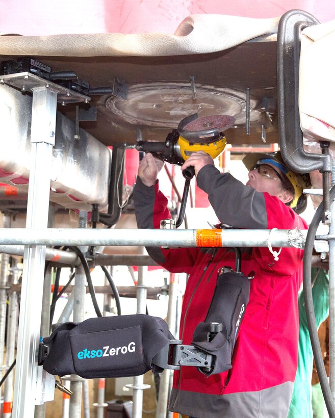 A Puget Sound Naval Shipyard & Intermediate Maintenance Facility worker demonstrates to managers, process improvement specialists and trades people how the Ekso zeroG Arm can be used to reduce injuries and increase productivity during a technology trial Feb. 26-28 at the shipyard in Bremerton, Washington. For the demonstration, the grinder was supported by the arm, which was attached to the simulated bulkhead with switchable magnetic bases. The arm can support up to 42-pound tools and absorbs up to 25 percent of the tool’s vibration. (U.S. Navy photo by Carie Hagins, PSNS & IMF photographer)