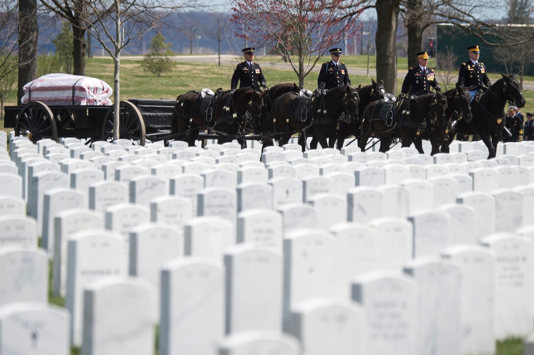 Service men on horses pull an American flag-covered casket through Arlington National Cemetery.