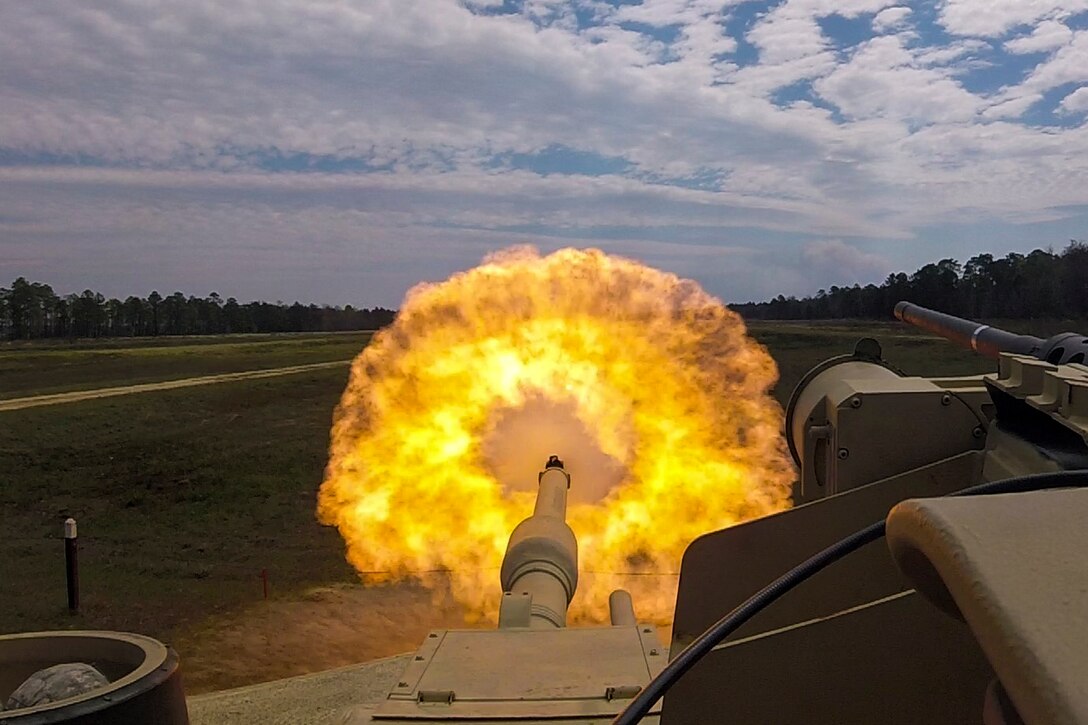 A fireball erupts out of the gun of a tank.