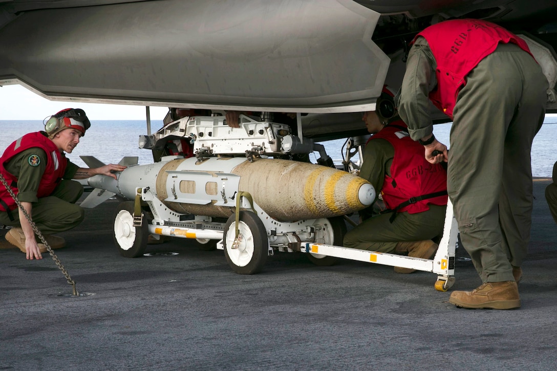 Marines mount a 1,000-pound guided bomb on an aircraft.