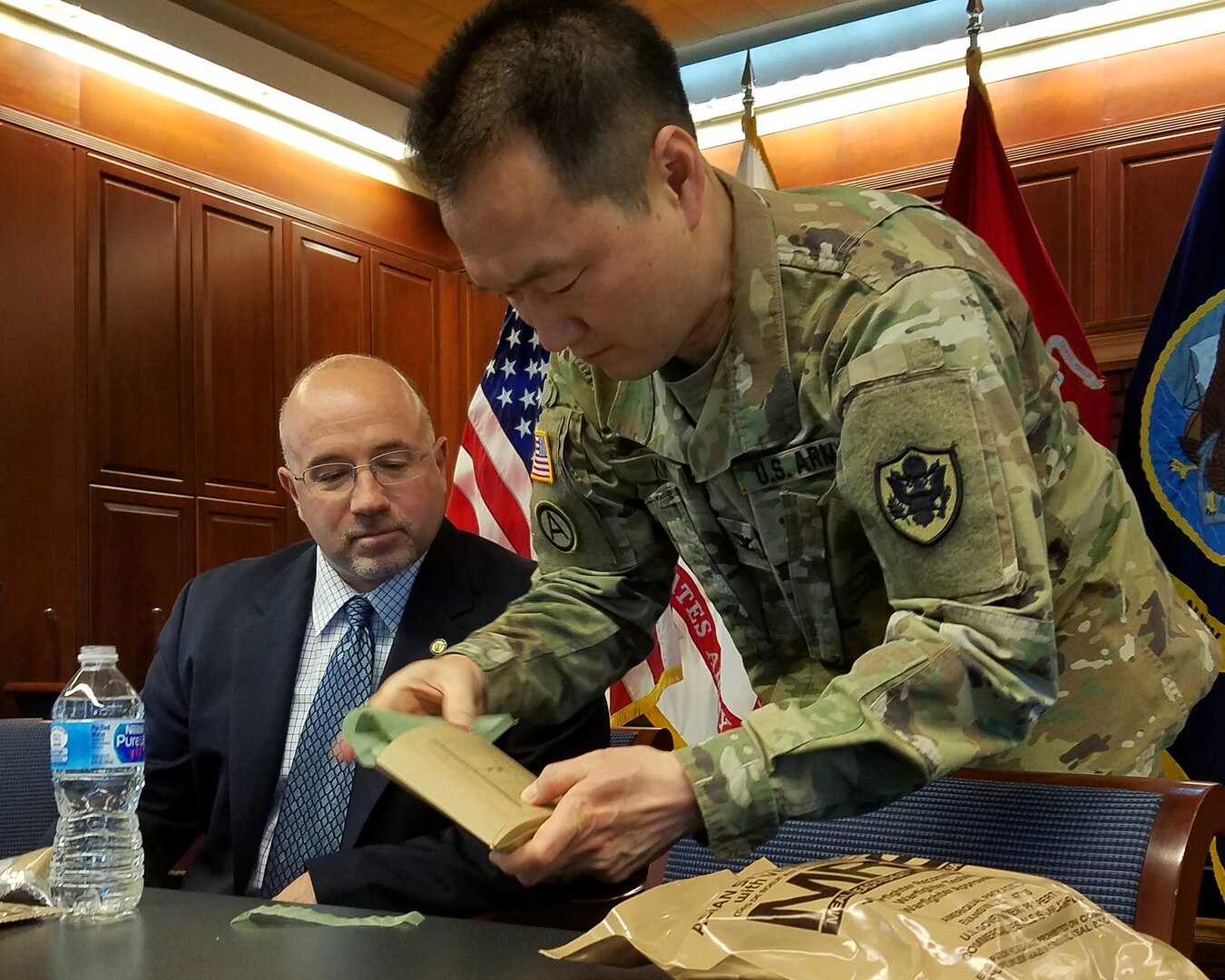 Army Col. Brian Kim, senior veterinary advisor, demonstrates the heater in a “meal, ready to eat” field ration for Mike Scott, deputy director of DLA Logistics Operations, at a lunch-and-learn event at DLA headquarters April 4. Scott hosted team members who learned about combat rations, tried current menus and taste-tested potential future products. Photo by Jacob Boyer