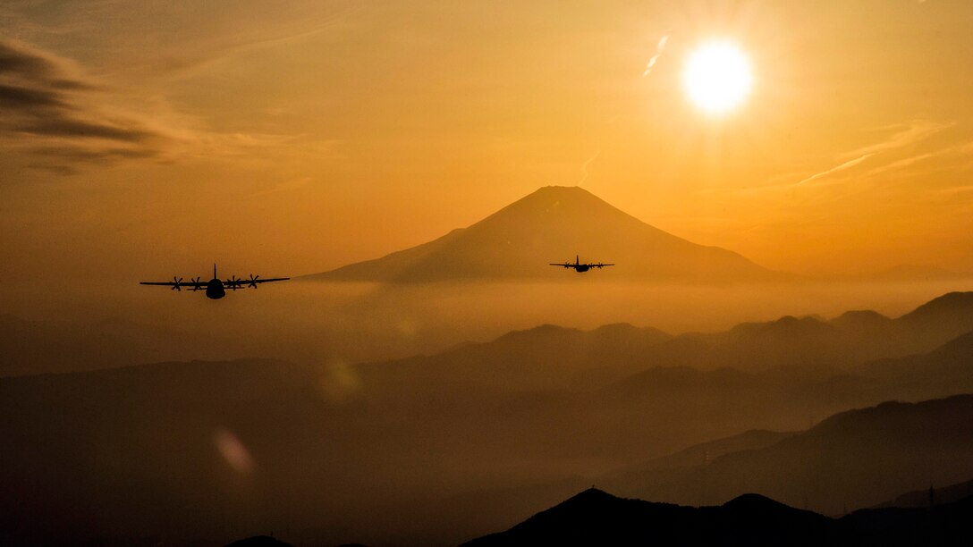 Two aircraft fly near a mountain against an orange sky.