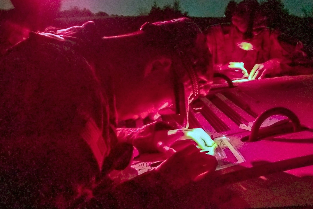 Soldiers, illuminated in pink light, study documents.