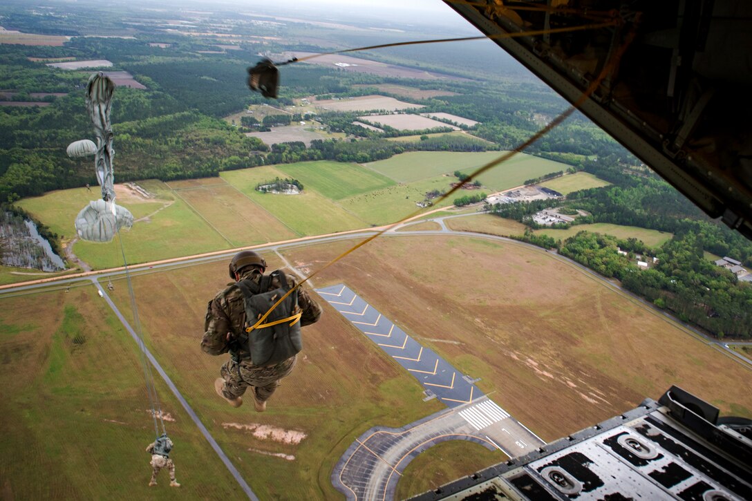 Airmen jump from an aircraft, and their parachutes begin to deploy.