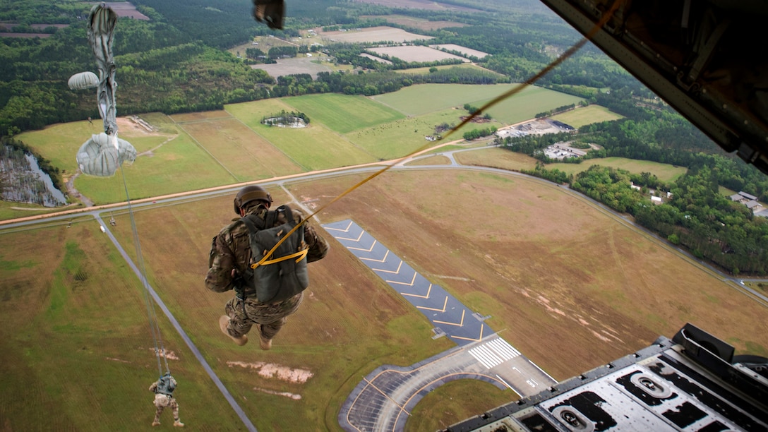 Airmen jump from an aircraft, and their parachutes begin to deploy.