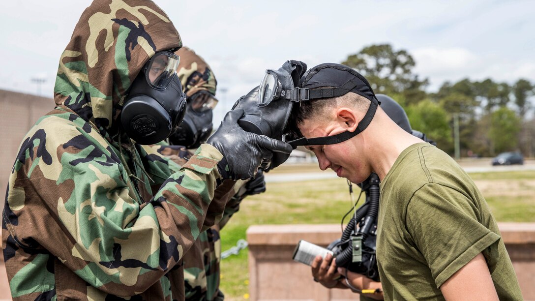 A Marine bows his head dwhile another service member takes off his gas mask.