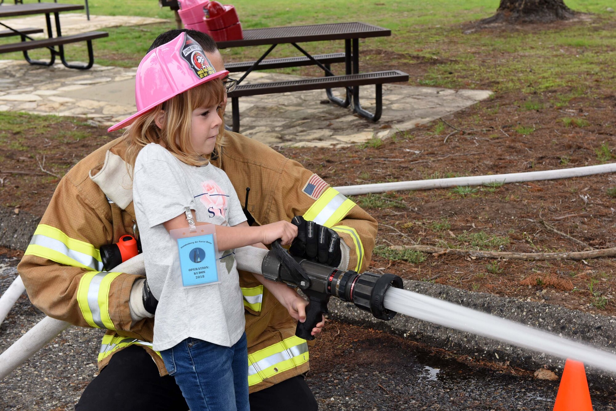 A military child uses a firefighter hose during Kids Understanding Deployment Operations, April 4, 2018, Vandenberg Air Force Base, Calif. KUDOS is a program developed to give children a deeper understanding of the military deployment process and equipment utilized during a deployment. (U.S. Air Force photo by Tech. Sgt. Jim Araos/Released)