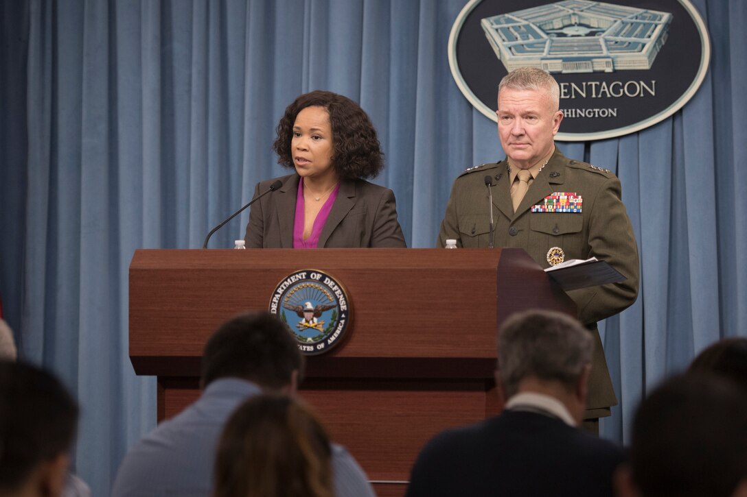 A civilian and a Marine general stand behind a podium.