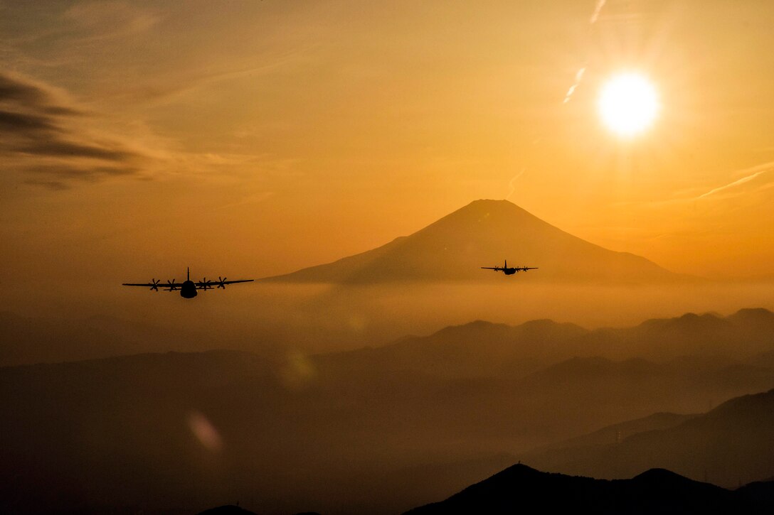 Two aircraft fly near a mountain against an orange sky.