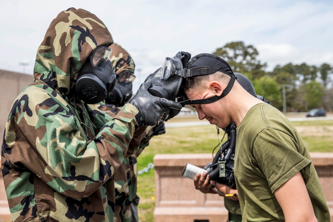 A Marine bows his head dwhile another service member takes off his gas mask.