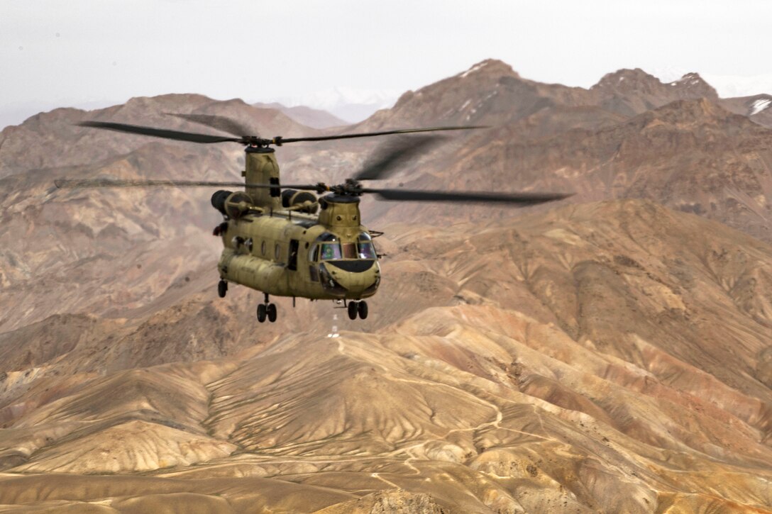 A CH-47F Chinook helicopter flies over Afghan mountains.
