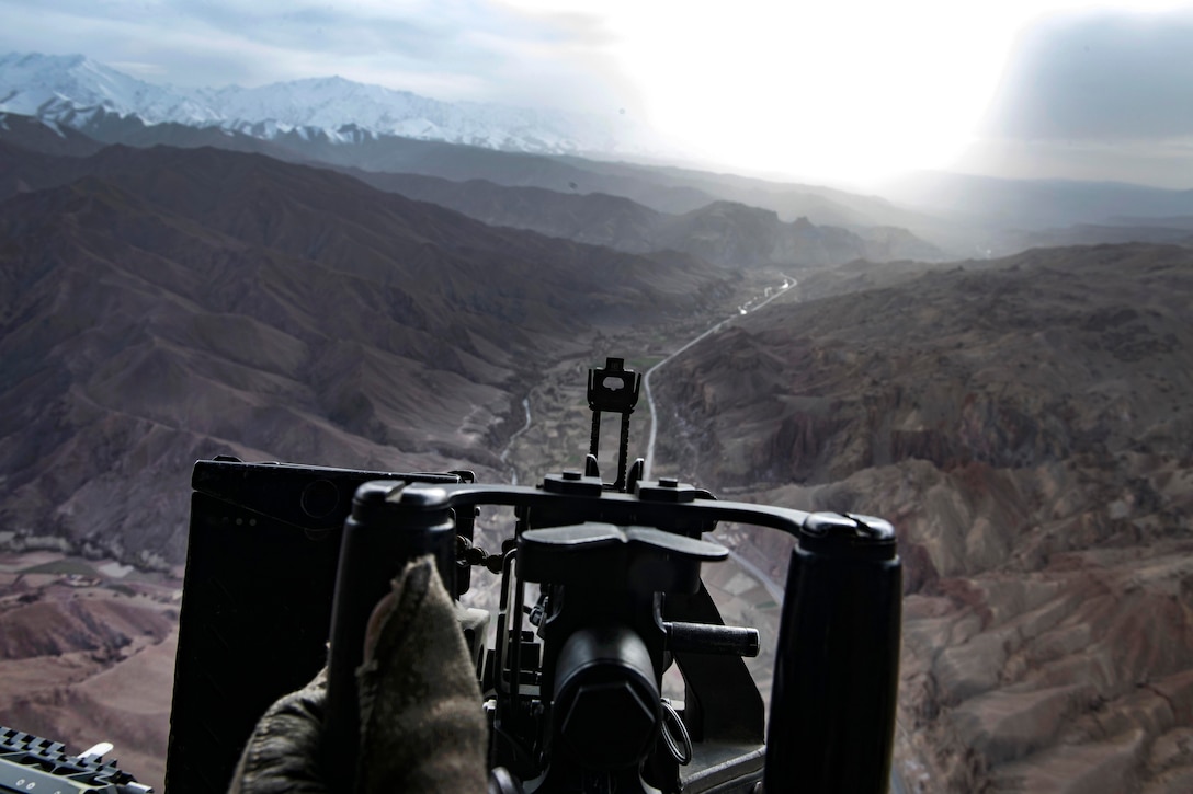The muzzle of an M240B machine gun is silhouetted by Afghan foothills.
