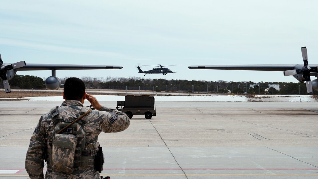 An airman salutes a passing HH-60G Pave Hawk helicopter.