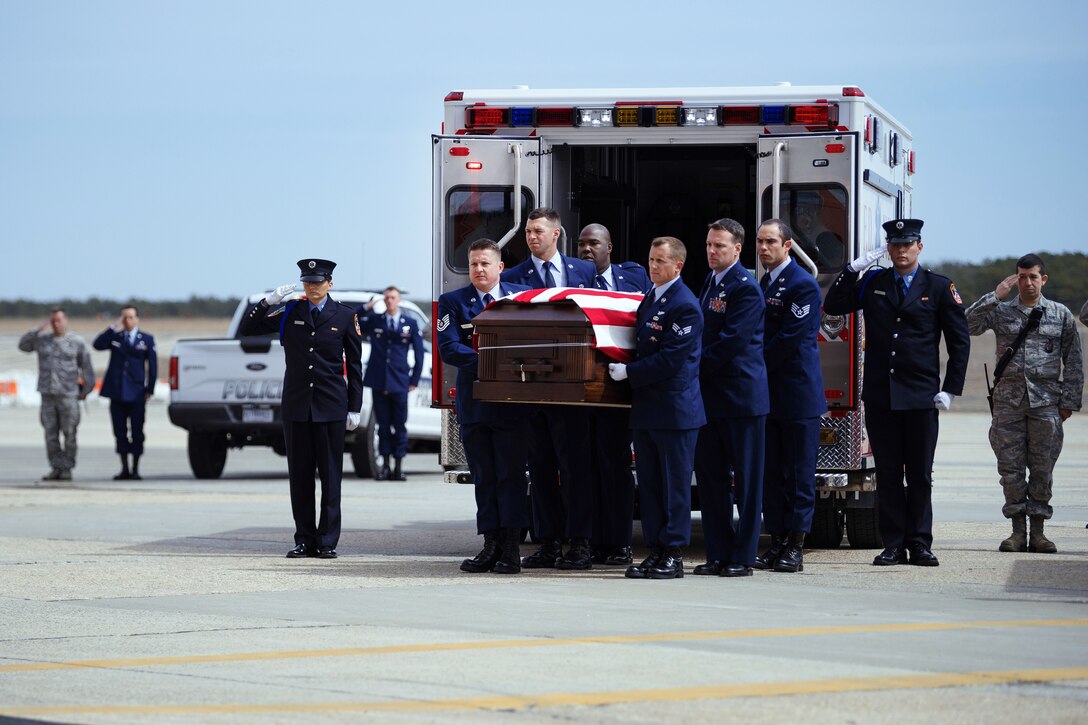 Airmen carry a flag-covered coffin from an ambulance.
