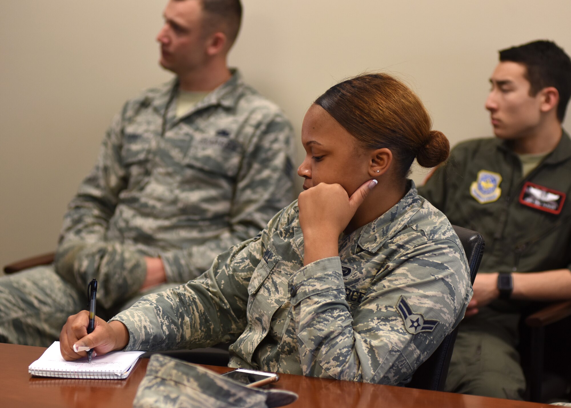 A female in uniform sits at a table taking notes.