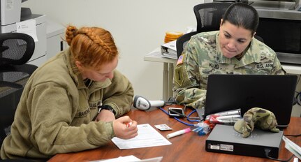 Army Staff Sgt. Amy Klug (right), noncommissioned officer in charge of the Akeroyd Blood Donor Center, registers Army Pvt. Angelica Sanchez in the donor center’s computer system. Sanchez, a combat medic student with Company E, 232nd Medical Battalion, is training at the Soldier Medic Training Site.