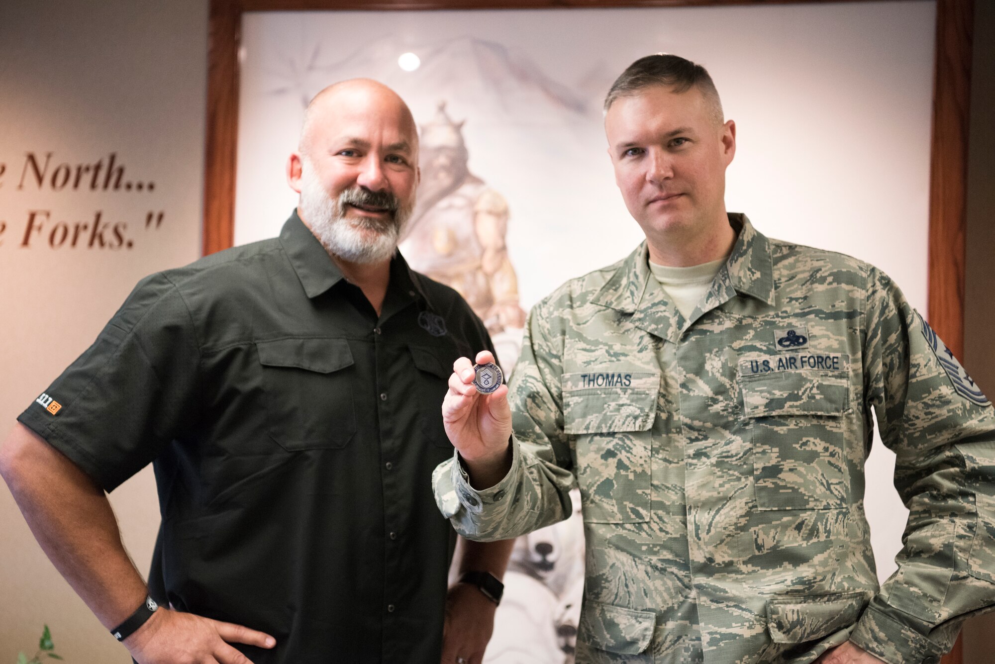 Chief Master Sgt. Brian Thomas, 319th Air Base Wing command chief (right), presents his chief coin alongside mentor and friend, (ret.) Chief Master Sgt. Calvin Markham, March 23, 2018, at Grand Forks Air Force Base, N.D. Markham gifted Thomas this coin when Thomas pinned on chief in 2013. (U.S. Air Force photo by Airman 1st Class Elijaih Tiggs)