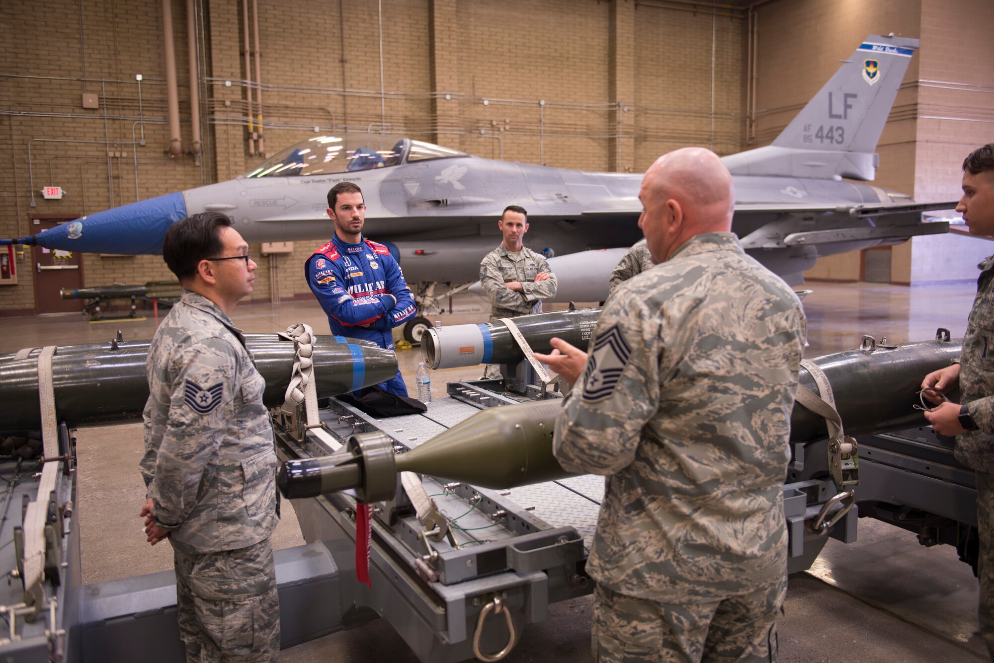 Alexander Rossi, Andretti Autosport racecar driver, listens as Chief Master Sgt. Daniel Gregory, 56th Maintenance Group superintendent, and other members of the 56th MXG, talk about aircraft weapons and ordnance at Luke Air Force Base, Ariz., April 5, 2018. Rossi’s visit raised awareness of the manpower and resources that go into driving the mission at an Air Force base. (U.S. Air Force photo by Senior Airman Ridge Shan)