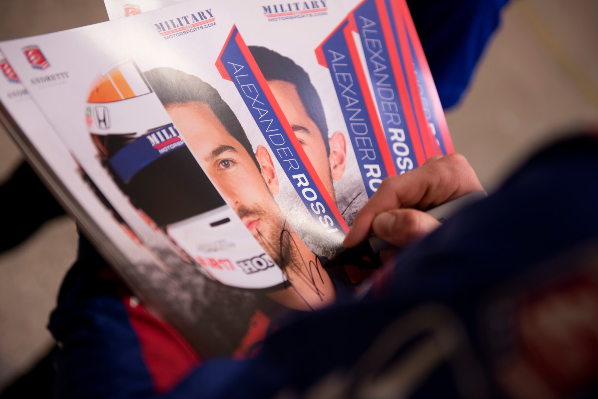 Alexander Rossi, Andretti Autosport racecar driver, autographs photos of himself to hand out to Airmen at Luke Air Force Base, Ariz., April 5, 2018. Rossi visited the base as part of a small delegation from Andretti Autosport in order to learn more and the mission and Airmen here. (U.S. Air Force photo by Senior Airman Ridge Shan)