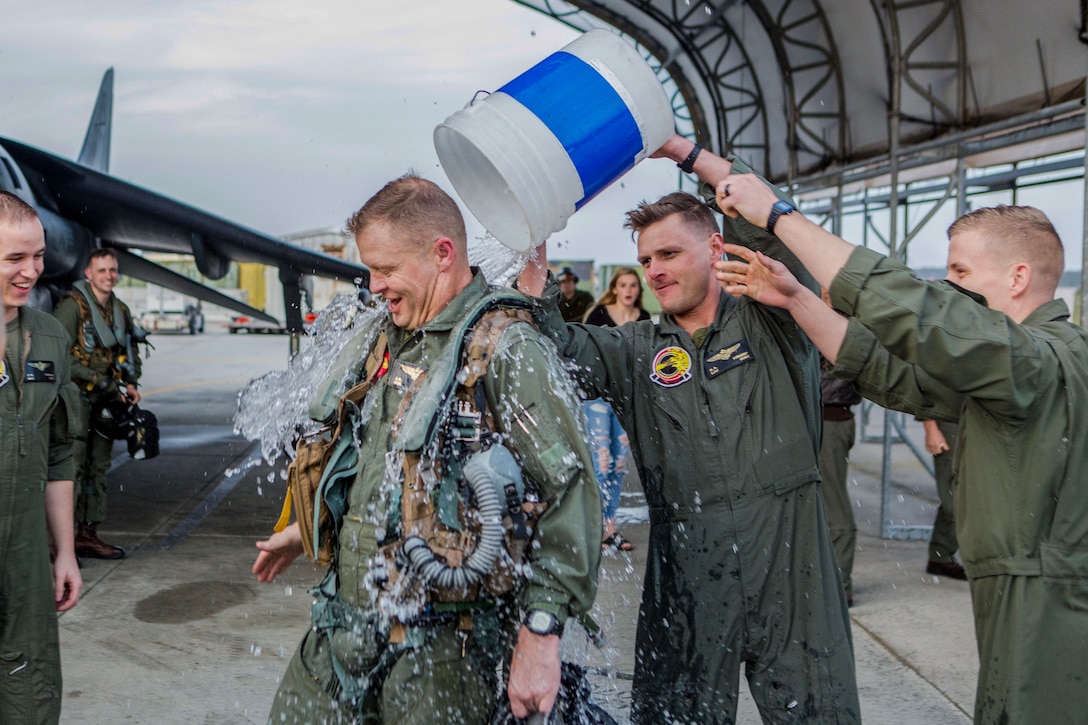 Marines pour a large bucket of water on a fellow Marine on a flightline.