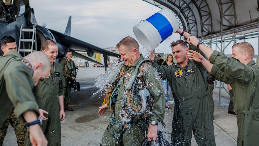 Marines pour a large bucket of water on a fellow Marine on a flightline.