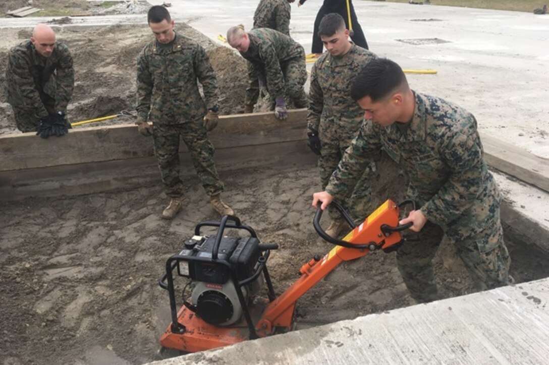 On March 19, 2018 Second Lieutenant Juan Gonzales, a Marine attending Combat Engineer Officer course 2-18 (CEO 2-18) at Marine Corps Engineer School aboard Camp Lejeune, N.C.; operates a compactor over an expedient crater repair. Pictured from left to right: Second Lieutenants Jon Roberts, Trevor Kenahan, Bethany Koshak, Thomas Raymond, and Juan Gonzales.
