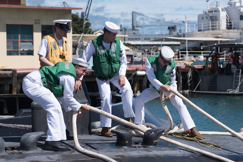 Sailors pull on ropes to bring a submarine to the dock.