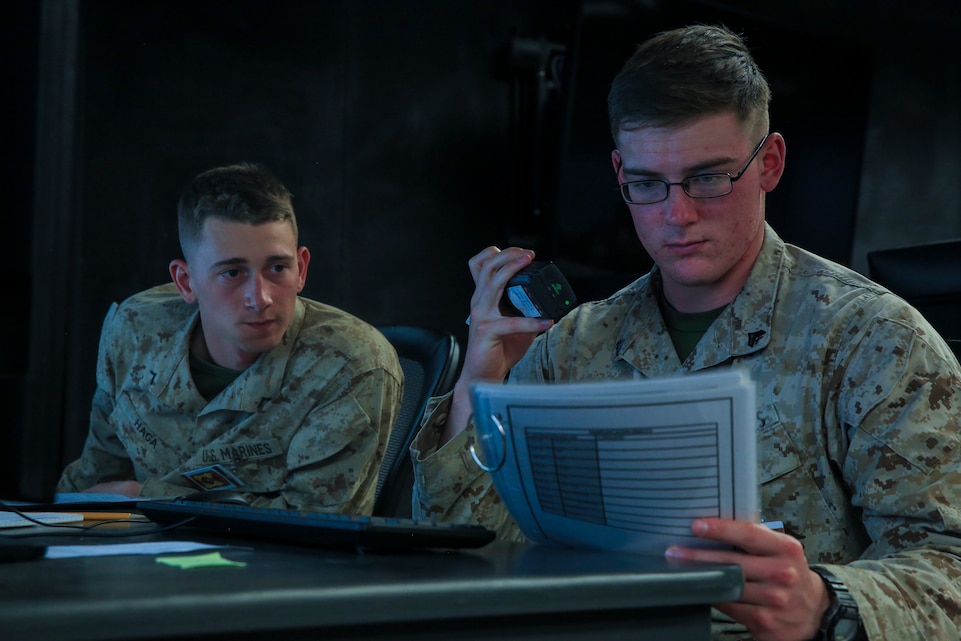 Pfc. Gage Haga, transmissions system operator, 1st Battalion, 4th Marine Regiment, stationed out of Marine Corps Base Camp Pendleton, Calif., watches while Cpl. Ryan Griffing, rifleman, 1/4, calls in a 9-line during Command Post Exercise 2 at the Battle Simulation Center aboard the Marine Corps Air Ground Combat Center, Twentynine Palms, Calif., March 29, 2018. CPX-2 is a is a two-part training event that focuses on training battalion staff and is a part of TALONEX 2-18, a pre-deployment training event that coincides with Weapons and Tactics Instructors Course. (U.S. Marine Corps photo by Lance Cpl. Isaac Cantrell)