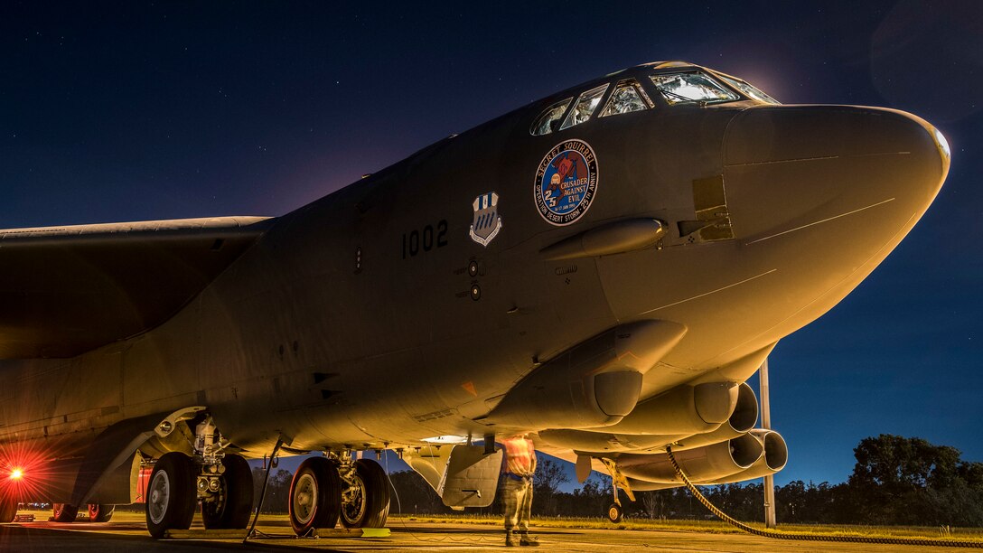 An Airman works beneath a B-52 aircraft, illuminated at night against a deep blue sky.
