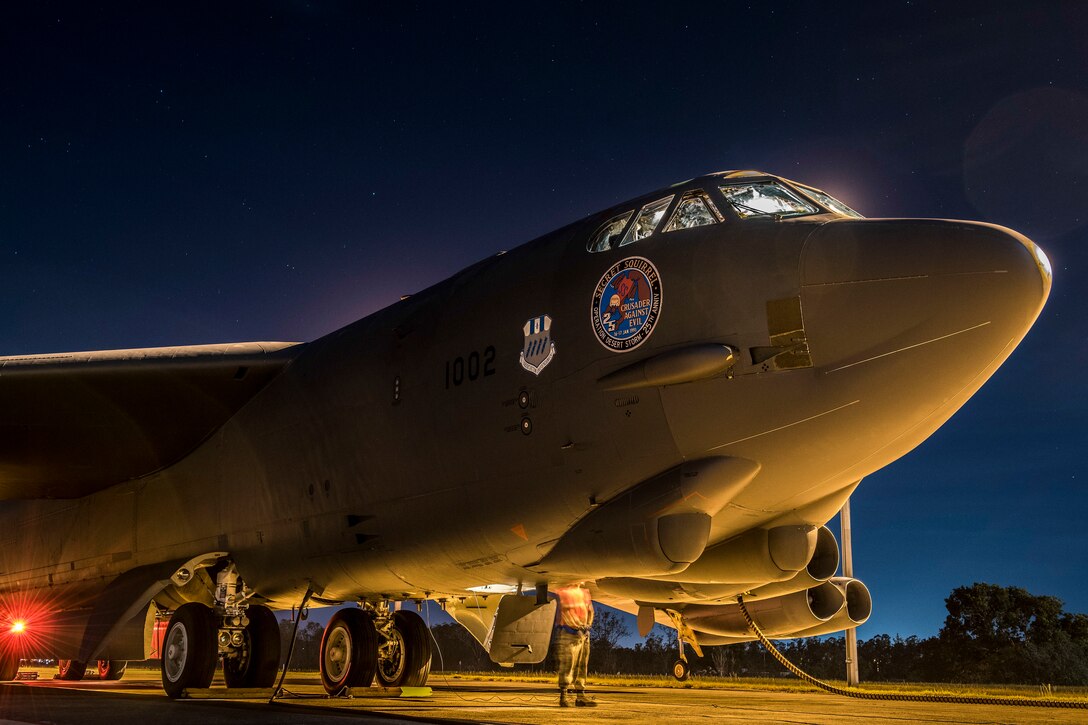 An Airman works beneath a B-52 aircraft, illuminated at night against a deep blue sky.