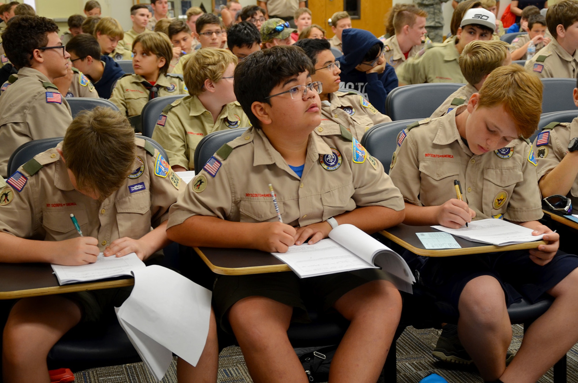 Jake Shipley (center), a 13-year-old Boy Scout from Hoover Middle School in Melbourne Beach, Fla., glances at PowerPoint slides as fellow scouts Ryan Herbruger (left) and Grand Newcombe (right) take notes during the Nuclear Science Merit Badge event hosted by the Air Force Technical Applications Center, Patrick AFB, Fla., March 31, 2018.  Shipley and his fellow scouts from Troop #330 earned the badge with the help of volunteers from the nuclear treaty monitoring center.  (U.S. Air Force photo by Susan A. Romano)