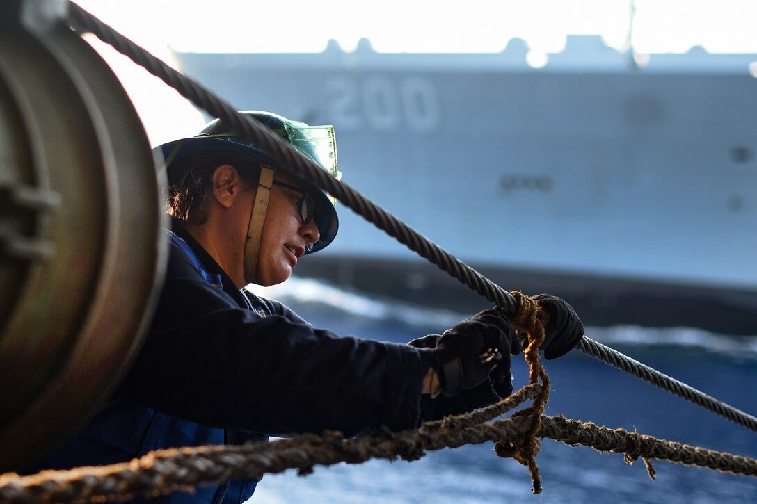 A sailor cuts through a rope stopper.