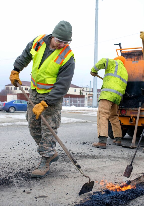 An airman lays asphalt while repairing potholes.