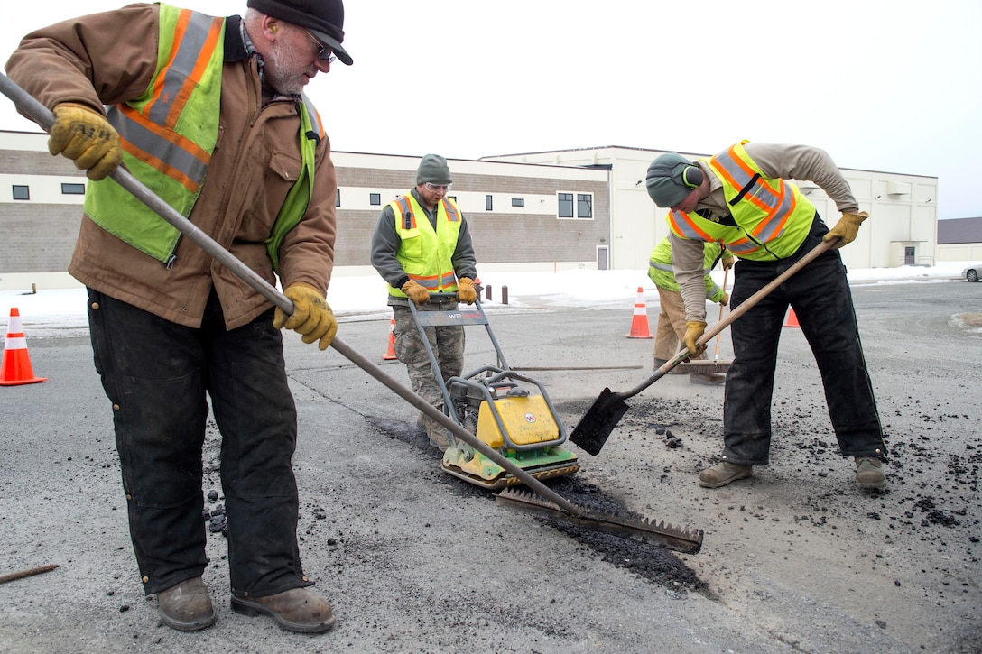 Airmen and civilians use a plate compactor to repair potholes.