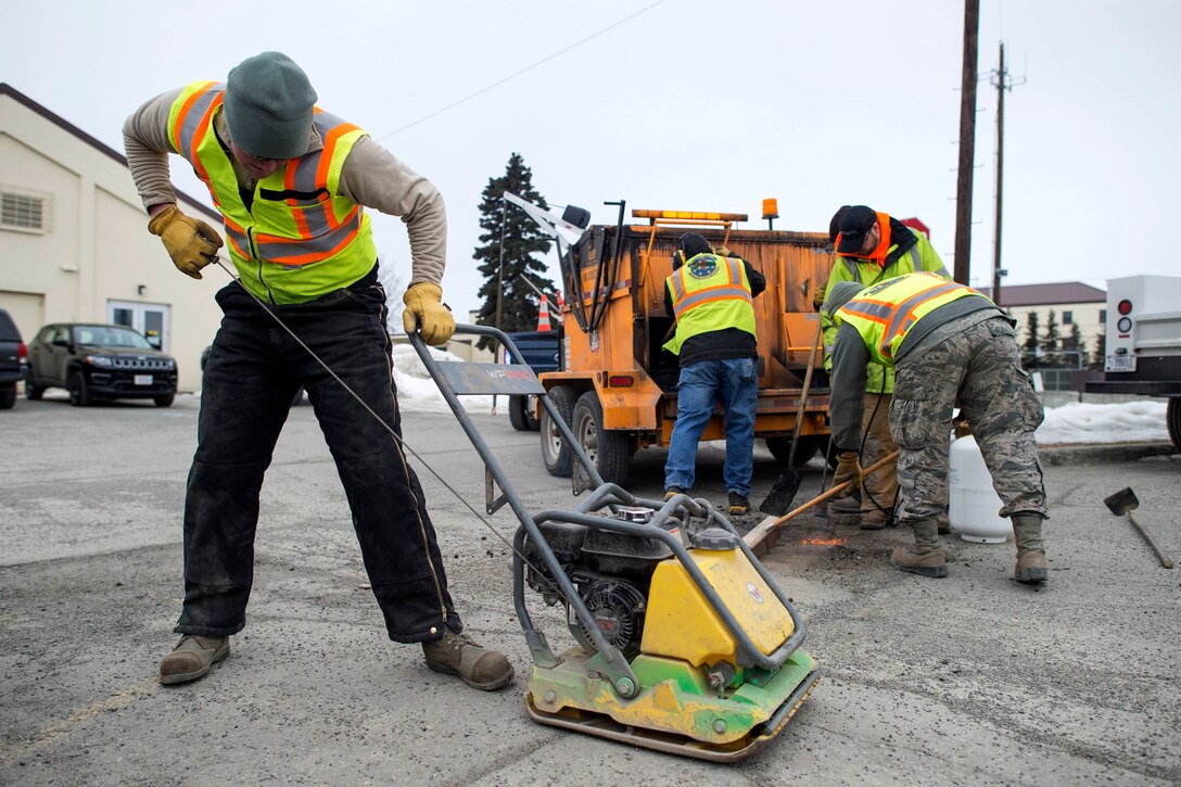 An airman uses plate compactor to repair potholes.