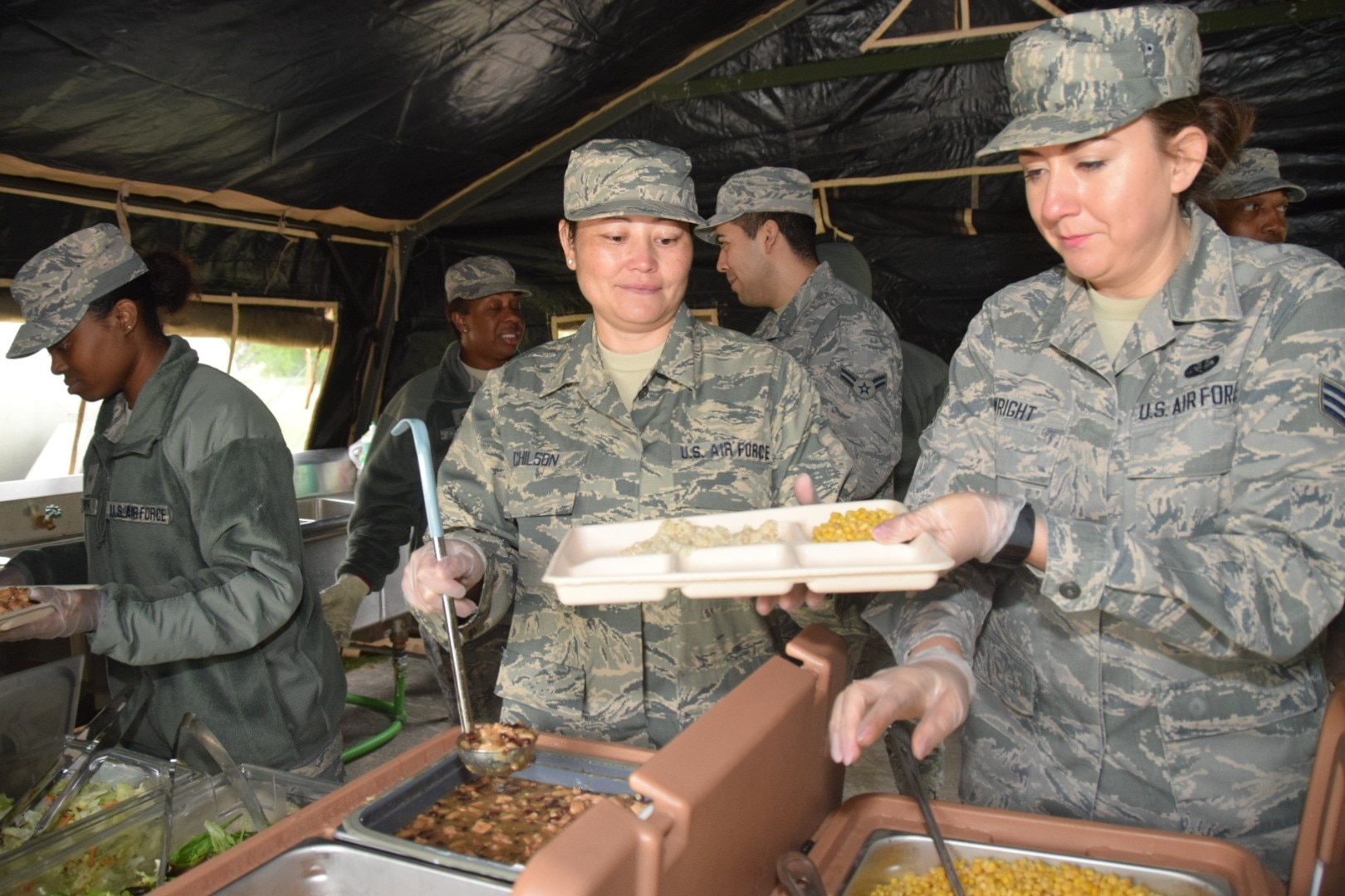 Senior Airmen Beatrice Chilson and Crystal Wright, 433rd Force Support Squadron, serve Unitized Group Rations for the first time in a Single Pallet Expeditionary Kitchen  April 7, 2018 during a field training on Joint Base San Antonio-Lackland, Texas. Chilson, a food service specialist, and Wright a fitness specialist, served a lunch consisting of southwestern chicken, white rice, garden salad, fruit cocktail and red velvet cake to Alamo Wing leadership. (U.S. Air Force photo by Tech Sgt. Carlos J. Treviño)