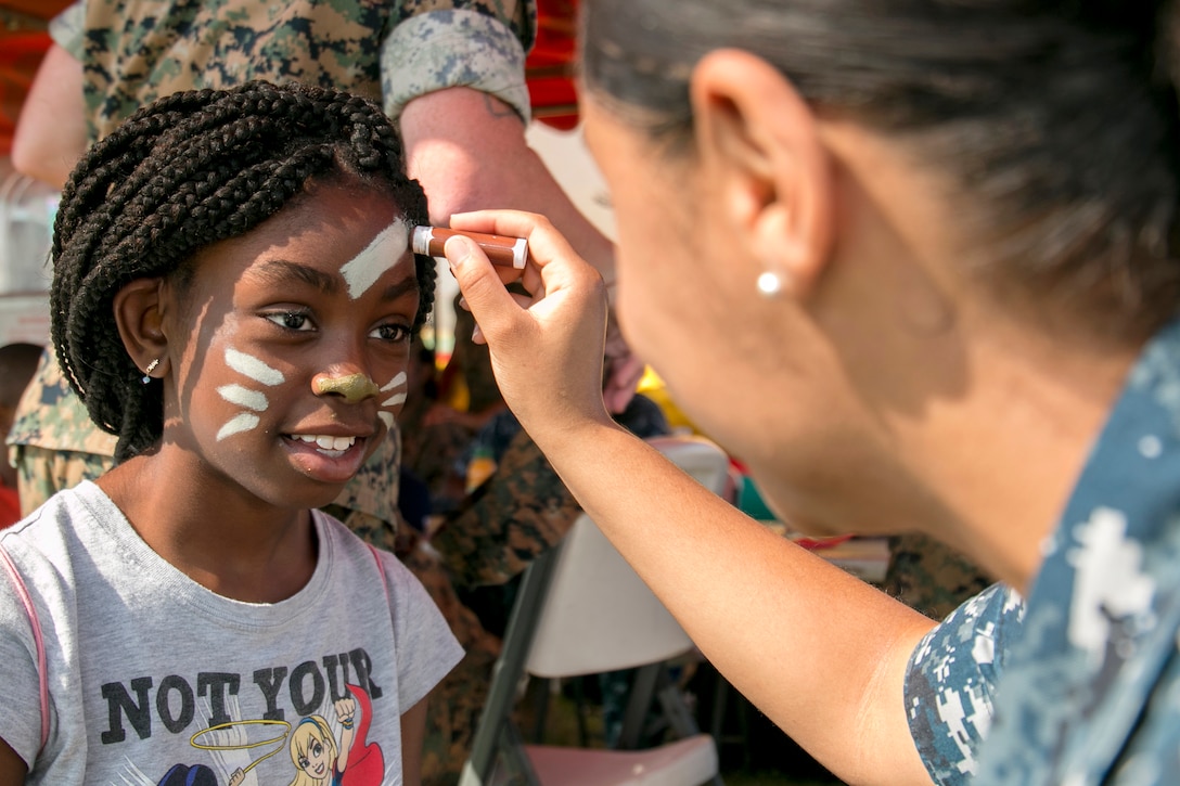 A sailor paints a child's face with paint.