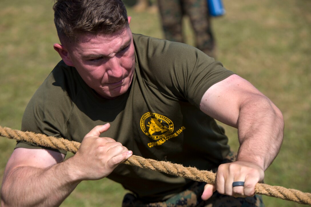 A Marine's face contorts and arm muscles strain as he pulls a rope.