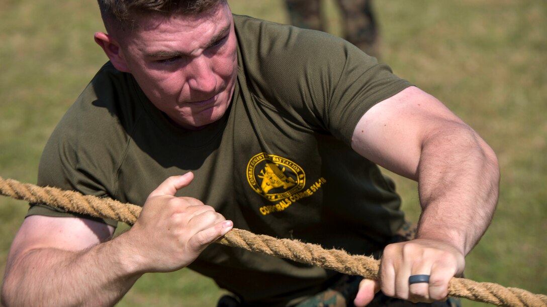 A Marine's face contorts and arm muscles strain as he pulls a rope.