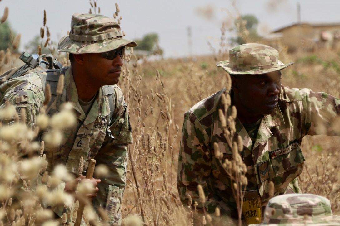 Soldiers in camouflage uniforms move through tall grass,