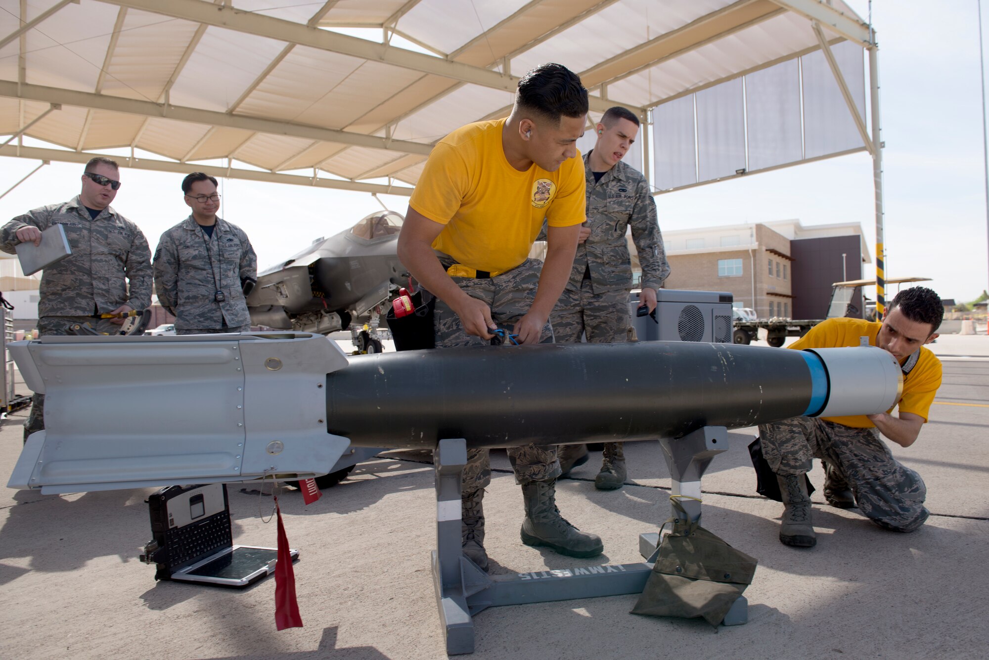 Airman 1st Class Ryan Tauoa, 61st Aircraft Maintenance Unit weapons load crew member, and Staff Sgt. Luis Santiago, 61st AMU weapons load crew lead, prepare an inert bomb for loading as judges observe during the 2018 1st Quarter Load Crew Competition at Luke Air Force Base, Ariz., April 6. Six teams from different AMUs competed to load F-16 Fighting Falcons and F-35 Lightning IIs. (U.S. Air Force photo by Senior Airman Ridge Shan)