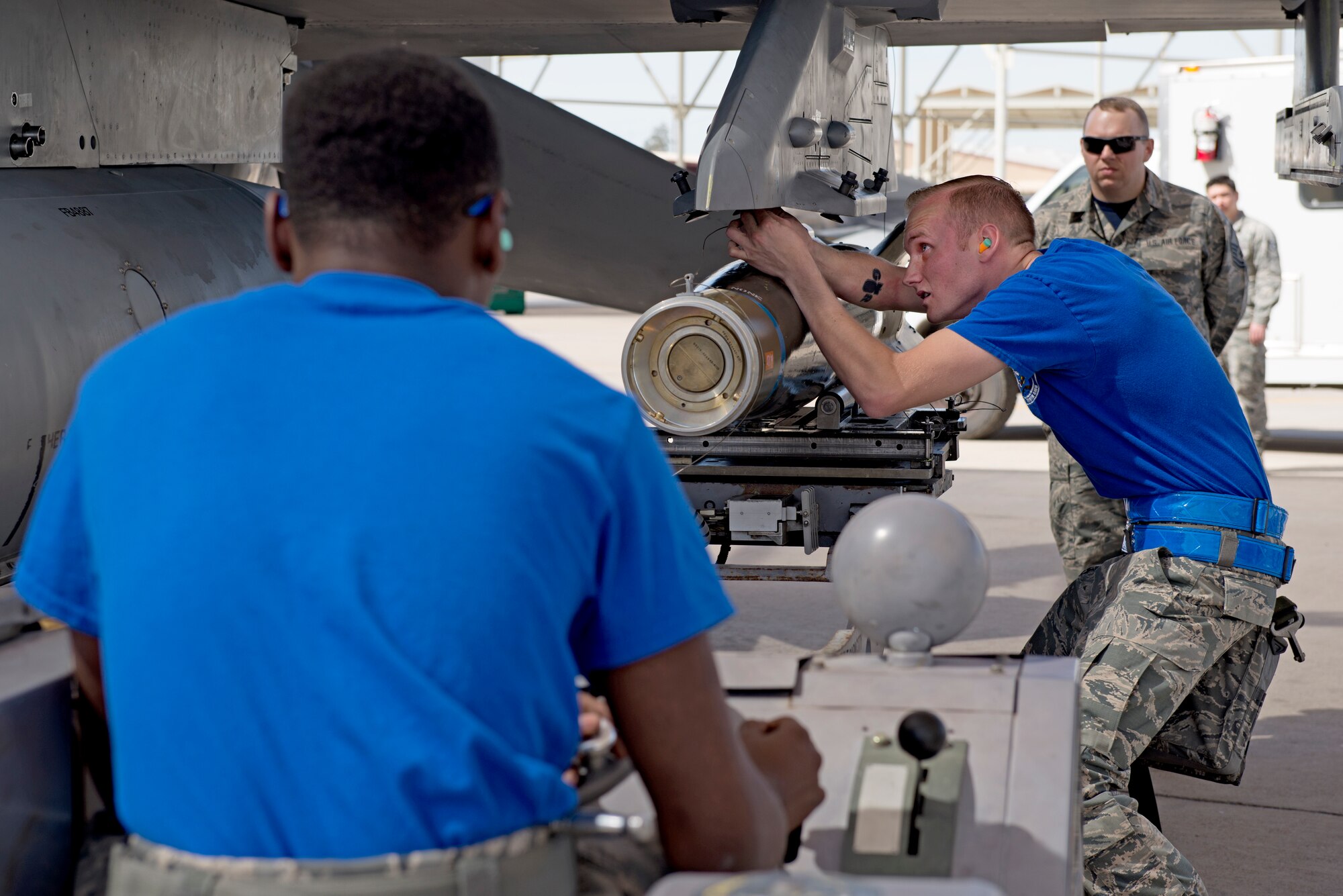 Airman 1st Class Jaylen Burton, 309th Aircraft Maintenance Unit weapons load crew member, raises an inert bomb with a utility lift while Staff Sgt. Cameron Platt, 309th AMU weapons load crew lead, attaches it to a pylon on an F-16 Fighting Falcon during the 2018 1st Quarter Load Crew Competition at Luke Air Force Base, Ariz., April 6. Along with the 310th and 425th AMUs, the 309th team competed to load F-16s while the teams from 61st, 62nd, and 63rd AMUs loaded F-35 Lightning IIs. (U.S. Air Force photo by Senior Airman Ridge Shan)